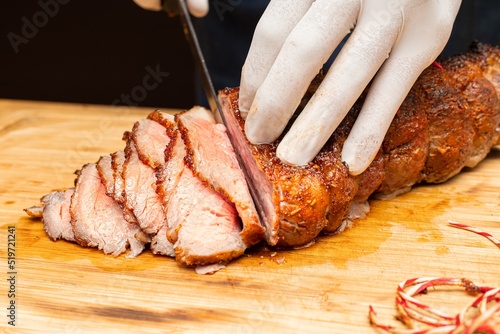 фотографія Closed up of chef’s hand slicing tender smoked and grilled beef on wooden board