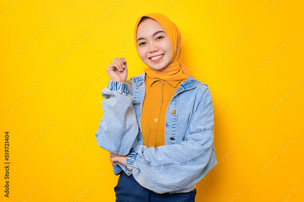 Happy young Asian woman in jeans jacket smiling pleased and looking confident isolated over yellow background Happy young Asian woman in jeans jacket smiling pleased and looking confident isolated over yellow background