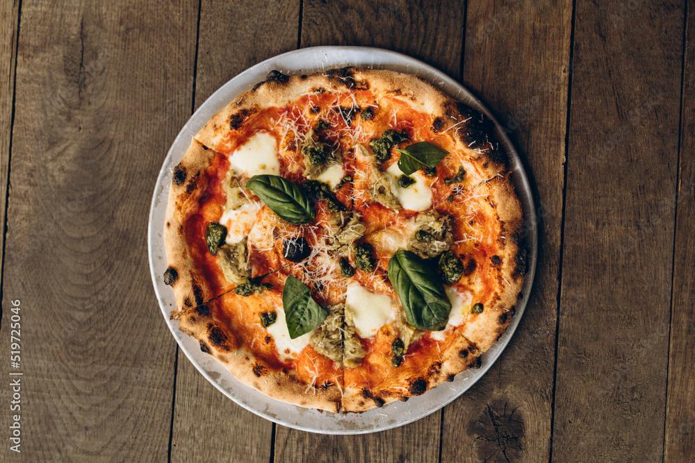 italian pizza with burnt sides on a wooden background top view. pizza with pesto sauce, mozzarella and basil leaves. sliced pizza close-up	