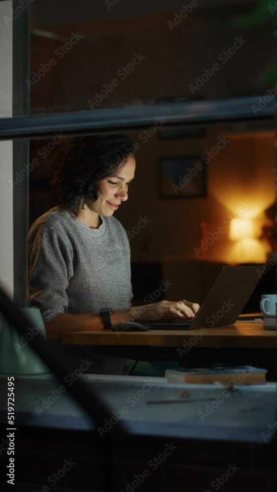 Vertical Screen: Brazilian Woman Sitting in front of Laptop Remotely Working on a Project. Happy Professional Working on Computer From Home. Productive From Home Worker. Shot Through Apartment Window. Vertical Screen: Brazilian Woman Sitting in front of Laptop Remotely Working on a Project. Happy Professional Working on Computer From Home. Productive From Home Worker. Shot Through Apartment Window.