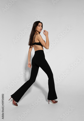 Full length image of a beautiful brunette young woman dressed in a black bra and pants, isolated white background.