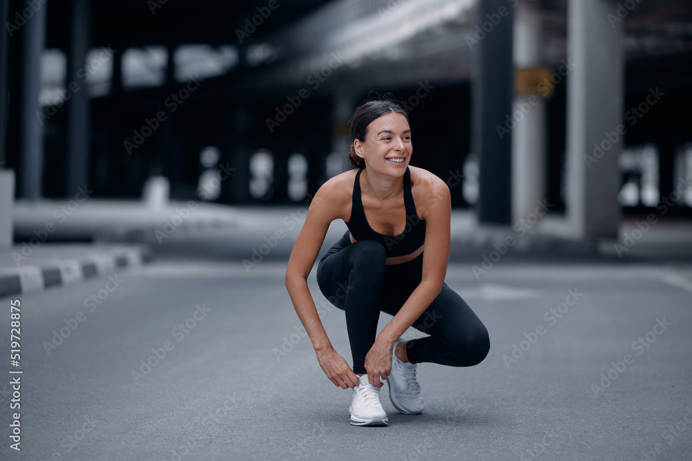 Female runner sitting outdoors and tying a shoelace on her sneaker. A runner getting ready for running Female runner sitting outdoors and tying a shoelace on her sneaker. A runner getting ready for running