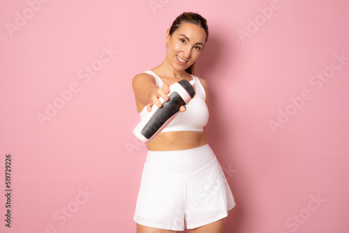 Healthy and Fitness concept - beautiful brunette girl in sport clothes drinking water after workout. Isolated on pink studio background