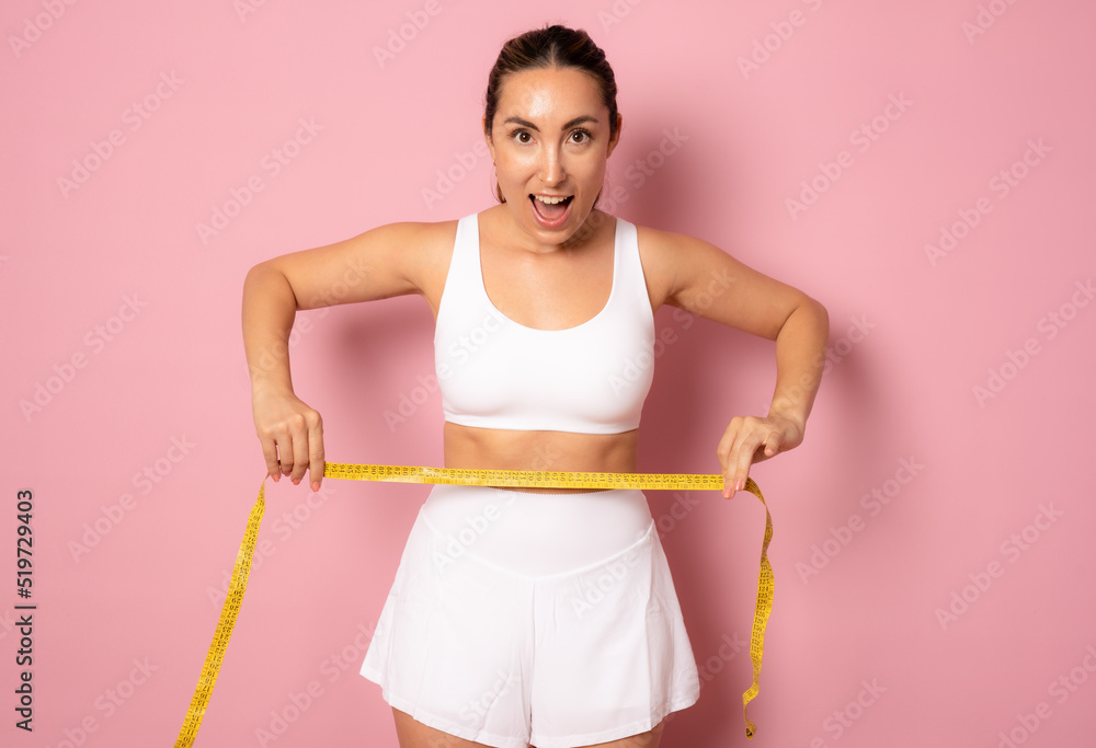 Weight Loss And Healthy Lifestyle Concept. Smiling slim woman measuring her waist with yellow tape over pink background. Weight Loss And Healthy Lifestyle Concept. Smiling slim woman measuring her waist with yellow tape over pink background.