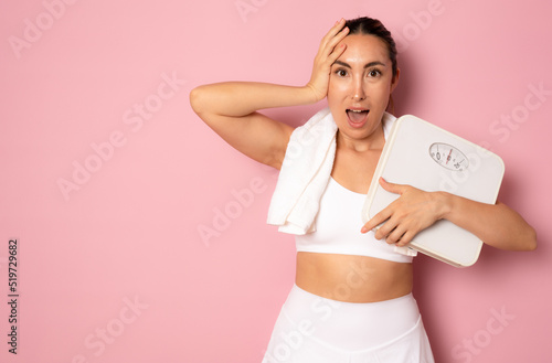 Worried young woman holding bathroom scales on pink background. Weight loss diet