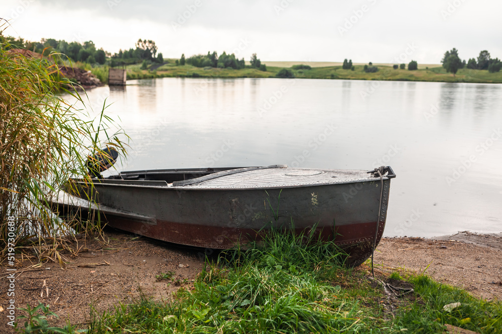 A motor boat is parked at the shore of a lake or river in the evening at sunset or early in the morning. The boat is in a quiet place next to the reeds and is ready for fishing. A motor boat is parked at the shore of a lake or river in the evening at sunset or early in the morning. The boat is in a quiet place next to the reeds and is ready for fishing.