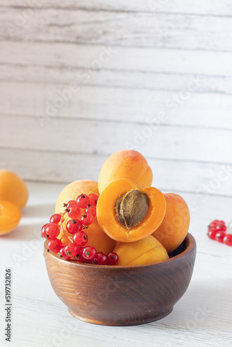 apricots and red currants in a wooden bowl on a white wooden background, apricot cut in half, fresh fruits and berries, copy space