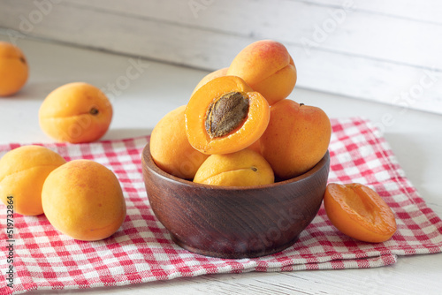apricots in a wooden bowl on a red checkered towel, apricot cut in half, fresh fruit