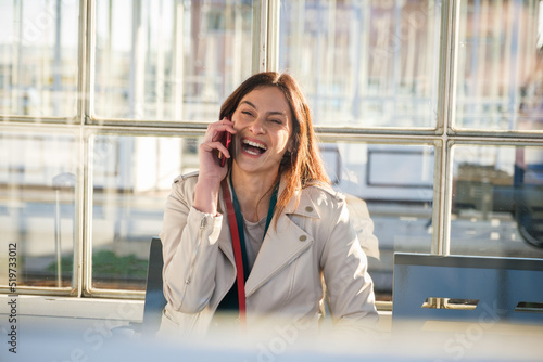 Young business woman waiting for the train sitting at the waiting room of train station - Cheerful and happy traveler talking on the smartphone while waiting for the train