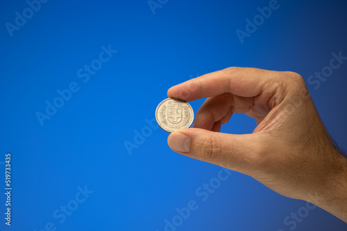5 Swiss Francs metal coin, held in hand by a Caucasian male. Close up studio shot, isolated on blue background