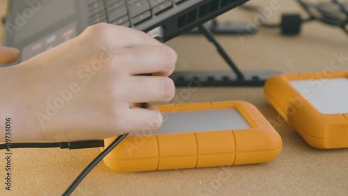 A hand connects an orange Lacie hard drive to a pc photo