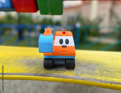 Closeup of the bright orange children's excavator with a cute smiling face. A portrait of the vivid toy excavator on the yellow wooden board. Friend