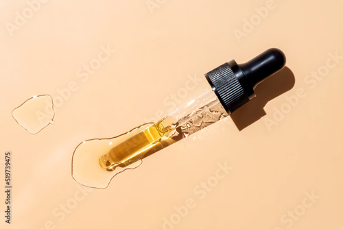 close up of pipette with pouring liquid serum and shadows on beige background. Trendy cosmetics shot with hard shadows. photo