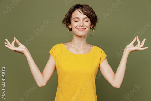 Young spiritual fun tranquil happy woman she 20s wear yellow t-shirt hold spreading hands in yoga om aum gesture relax meditate try to calm down isolated on plain olive green khaki background studio.