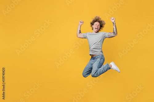 Full body happy excited overjoyed young caucasian man 20s he wearing grey t-shirt look camera jump high do winner gesture isolated on plain yellow backround studio portrait. People lifestyle concept.