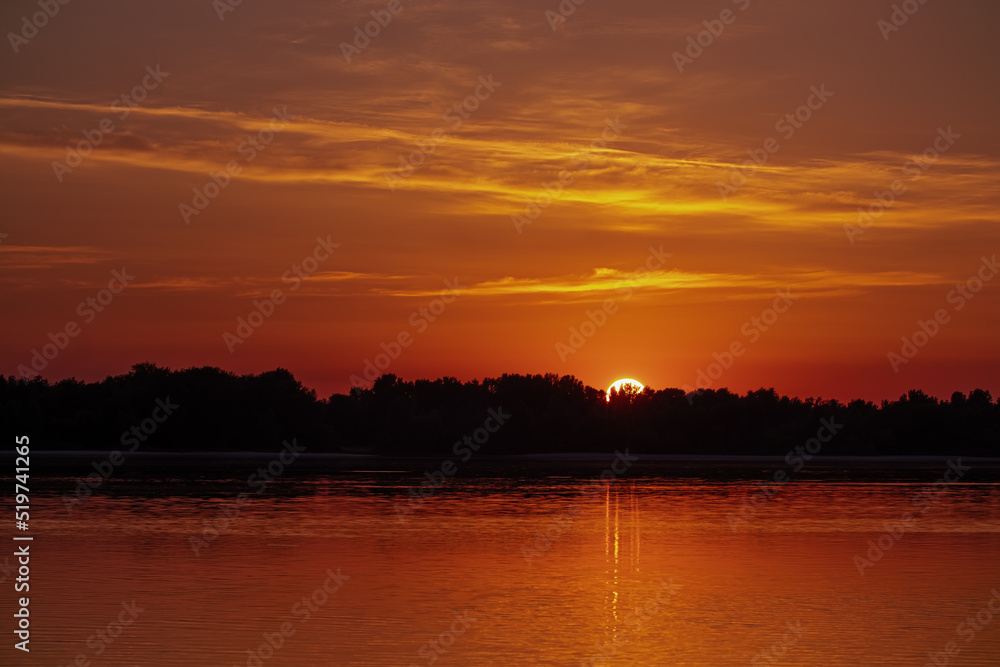 Golden sunset over the river. The sun sets over the horizon, hides behind the trees