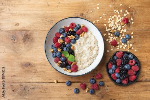 Oatmeal porridge in bowl with blueberry, nuts and raspberry on wooden table top view. Yummy and diet breakfast.