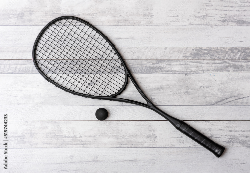Black squash racket and ball on grey court. Horizontal sport theme