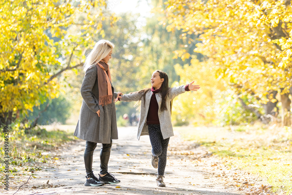 Fototapeta premium Little girl and her mother enjoy sunny weather in the autumn park