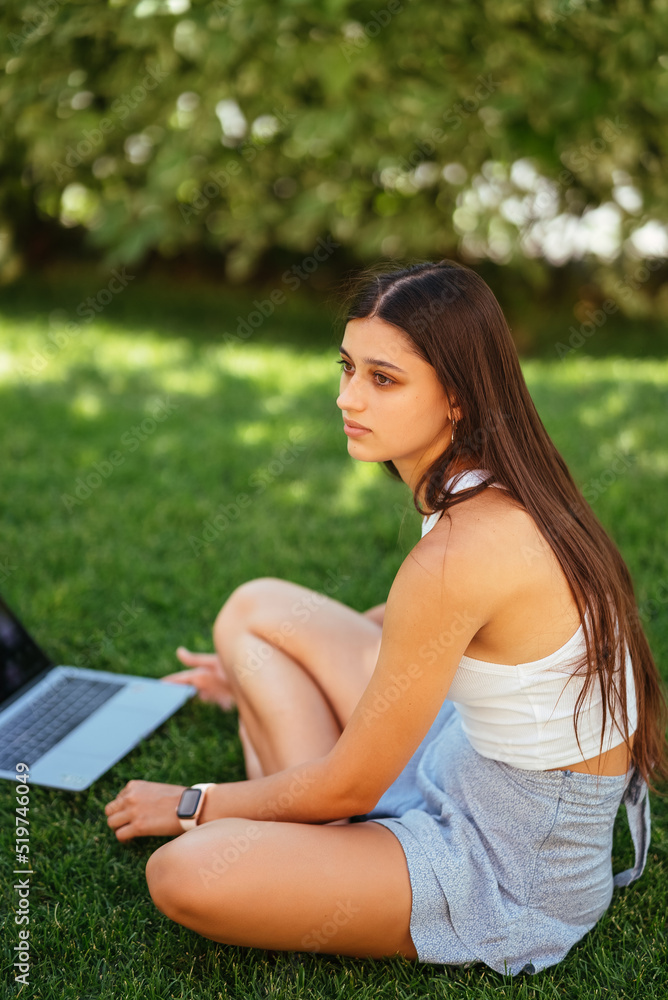 Young girl works with a laptop, sitting on the lawn. Young girl works with a laptop, sitting on the lawn.