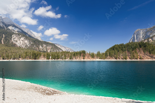 Fototapeta Naklejka Na Ścianę i Meble -  Transparent emerald water of lake Tovel framed by gently sloping shores and the Italian Alps under clear blue sky with occasional clouds, Ville d'Anaunia, Trentino