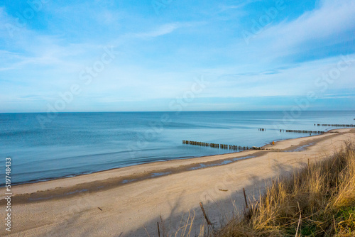 Beautiful sandy coast of baltic sea with breakwaters, minor clouds and deep blue sky