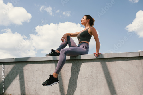 Portrait of young woman in sportswear taking a break during her workout. Sky background. Healthy habits.
