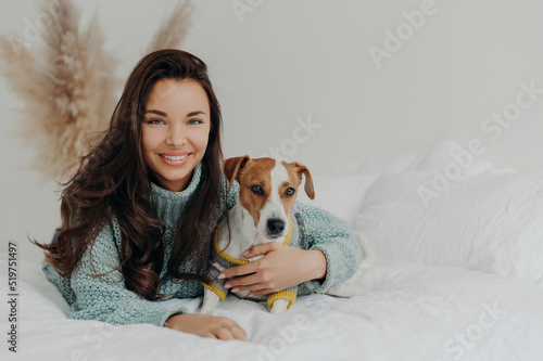 Photo of cheerful woman embraces dog with love, spend free time together, expresses tender feeling and emotions, falls in love with pet, lie on comfortable bed. Positive emotions, animals and care © VK Studio