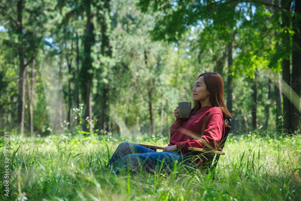 Portrait image of a beautiful young asian woman drinking coffee while sitting on a chair in the park Portrait image of a beautiful young asian woman drinking coffee while sitting on a chair in the park