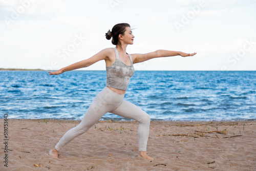 Woman practicing yoga outside in warrior pose on beach