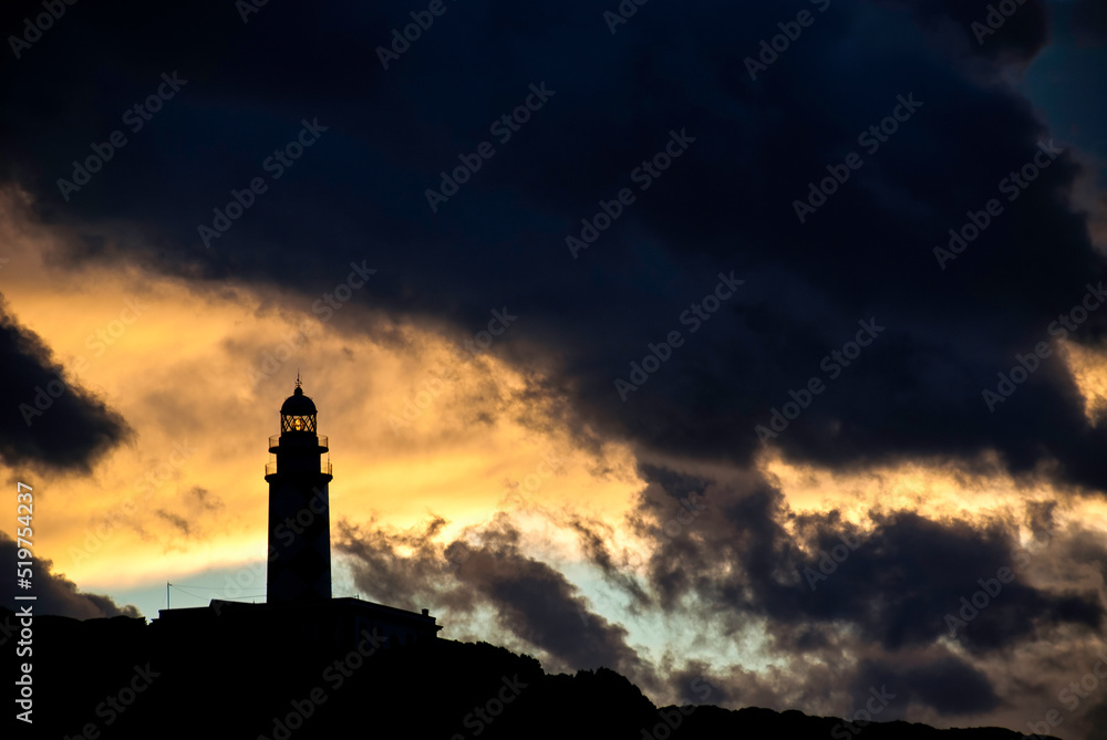 Silhouette of a lighthouse in a cloudy sky at sunset