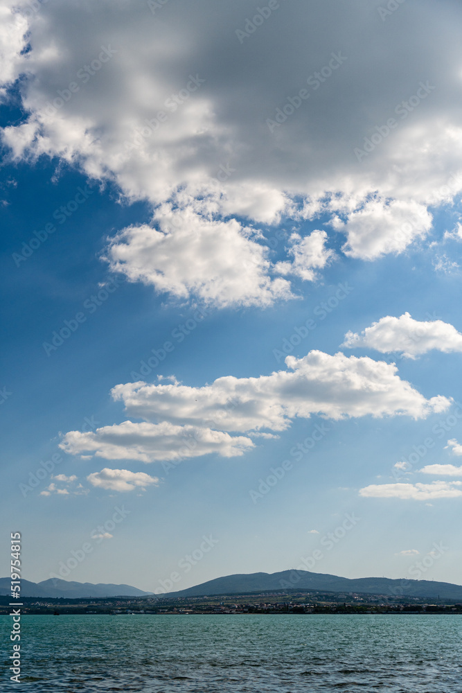 White beautiful clouds on endless expanses of Black Sea. Clouds on background of Caucasus mountains. Emerald sea water. Clouds are reflected in sea water. White beautiful clouds on endless expanses of Black Sea. Clouds on background of Caucasus mountains. Emerald sea water. Clouds are reflected in sea water.