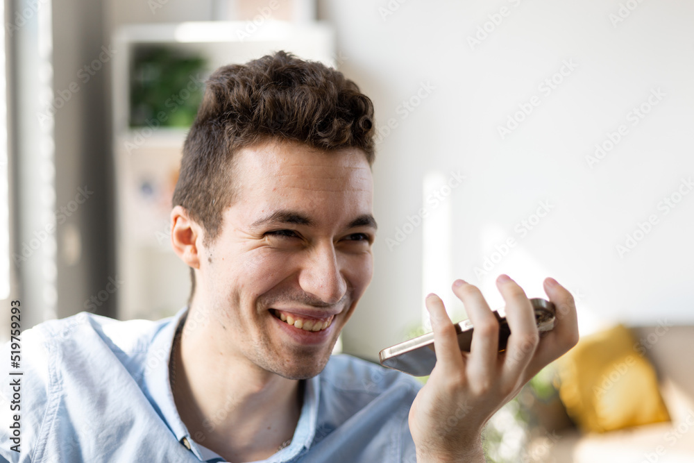 Modern tech in work. Focused male manager expert advisor using virtual assistant app on phone working by laptop in office. Young businessman hold phone by mouth use voice dialing or information search Modern tech in work. Focused male manager expert advisor using virtual assistant app on phone working by laptop in office. Young businessman hold phone by mouth use voice dialing or information search