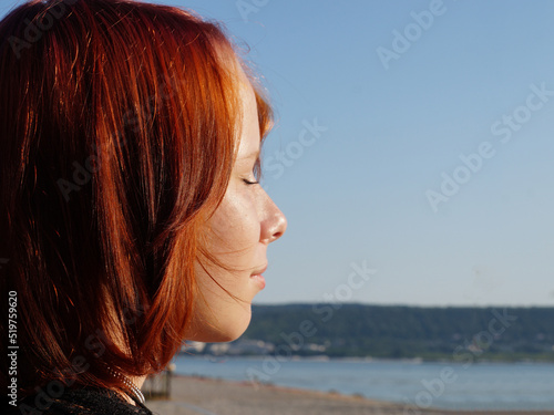 profile of a red-haired teenage girl with closed eyes close-up against the background of the sea, copy space