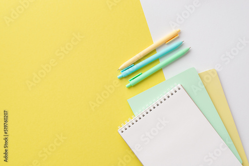 School concept. Top view photo of stationery notepads and colorful pens on bicolor yellow and white background with copyspace