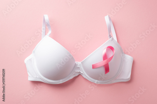 Breast cancer awareness concept. Top view photo of white brassiere with pink silk ribbon on isolated pastel pink background