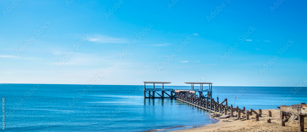 The landscape of tropical sandy beaches with sea and blue summer skies is beautiful with an old broken bridge leading to the sea.