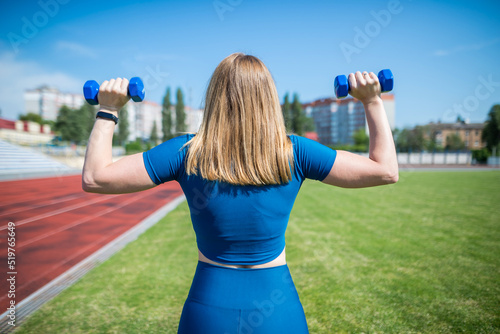 woman in the stadium with dumbbells, rear view