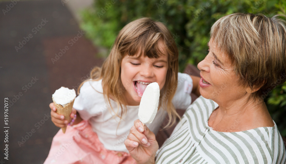 grandmother and child granddaughter eat ice cream in the park on a summer day. happy family has fun together in nature grandmother and child granddaughter eat ice cream in the park on a summer day. happy family has fun together in nature