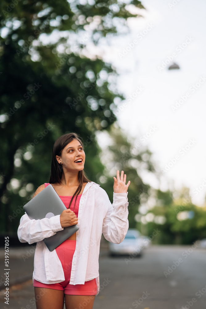 Young woman walking outdoors holding laptop computer Young woman walking outdoors holding laptop computer