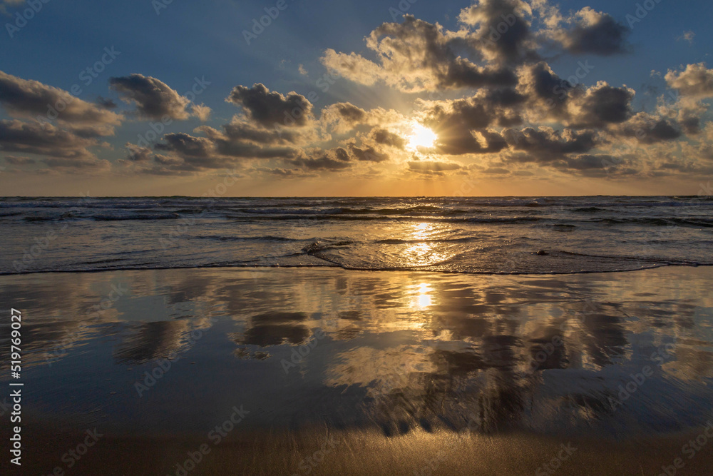 Sunset on the Mediterranean coast. Natural landscape. Mediterranean nature. Reflection, beautiful clouds, blue sky and yellow sunlight. Israel.