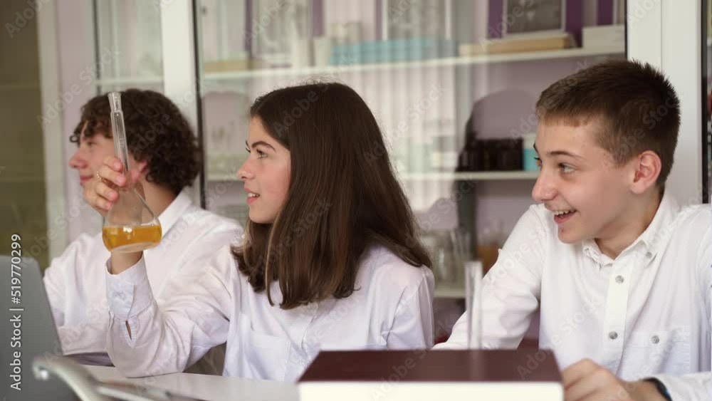 School education 4k video. Cheerful classmates in chemistry lesson hold flasks with liquid for experiments and smile and laughing. Happy friends study together in class in laboratory. School education 4k video. Cheerful classmates in chemistry lesson hold flasks with liquid for experiments and smile and laughing. Happy friends study together in class in laboratory.