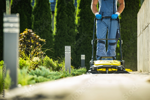 Obraz na płótnie Landscaper Worker with Push Sweeper Cleaning Garden Pathway