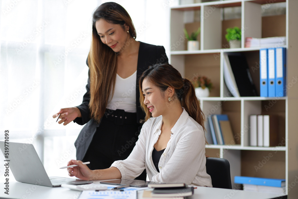 Fototapeta premium Attractive Asian businesswoman and secretary colleague discussing working on a business project at an office desk.