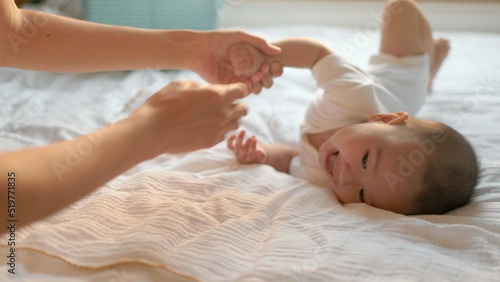 Mother helps to turn over to her baby boy on big bed. Baby's turn over exercises 