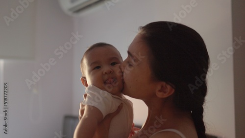 Happy mother is holding her baby and kissing with love at home