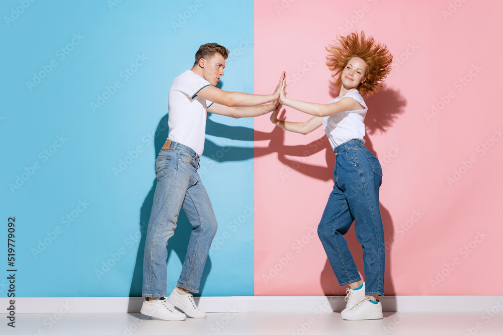 Fototapeta premium Portrait of young, emotive couple, man and woman, dancing, posing isolated over pink blue studio background