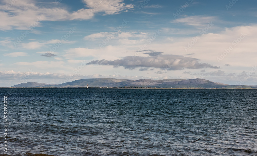 View on blue ocean water of Galway bay, Ireland. Burren mountains in the background. Soft pastel sky.