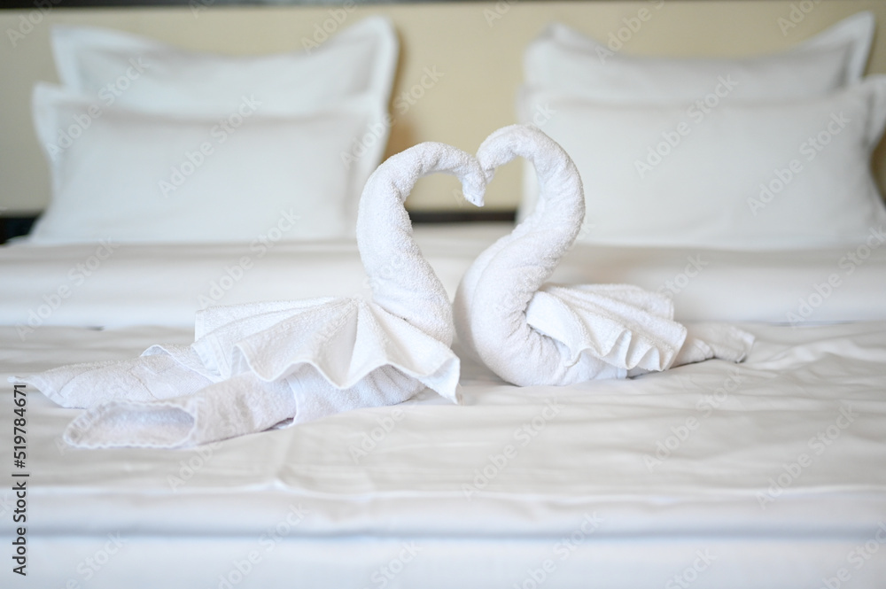 Obraz premium Swans made of white bath towel in hotel room. Decoration on bed in motel. Towel folded in swan shape.