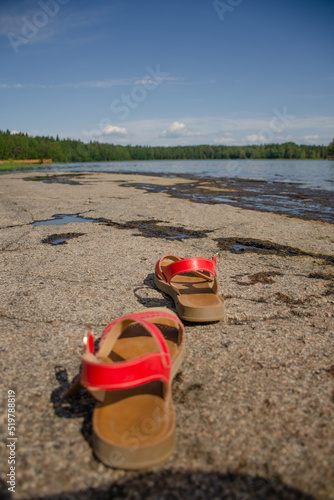 Red sandals on a stone shore in summer close-up. Vacation and travel concept